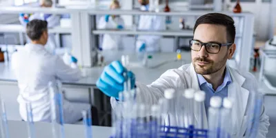 Scientist places a test tube into a rack. Another scientist sits at a bench in the background