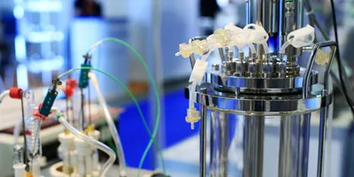 Stainless steel bioreactor with connected tubing and sensors in a biotechnology lab.