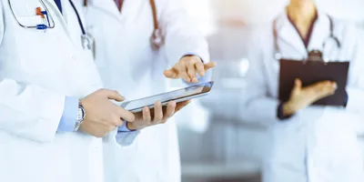 Pharmaceutical laboratory professionals in lab coats collaborating with a digital tablet and clipboard during equipment qualification procedures.