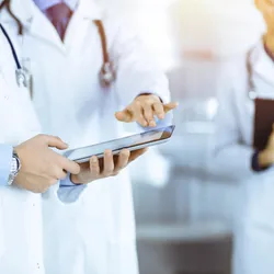 Pharmaceutical laboratory professionals in lab coats collaborating with a digital tablet and clipboard during equipment qualification procedures.