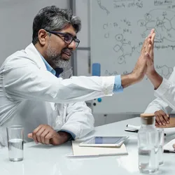 Lab managers and scientists in a meeting celebrating teamwork and collaboration, demonstrating strong lab leadership and positive lab culture.