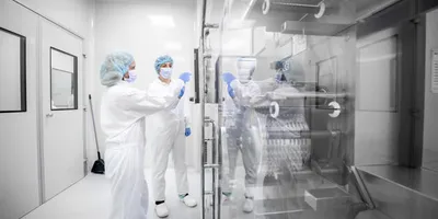 Pharmaceutical personnel in full cleanroom attire inspecting equipment inside a sterile, controlled environment with reflective surfaces and HEPA-filtered enclosures.