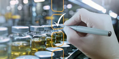 Gloved hand using a stylus to mark a checklist overlaid on a background of pharmaceutical vials filled with liquid on a production line.