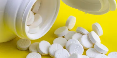 White prescription tablets spilling out of an open pill bottle onto a bright yellow surface, with visible dosage markings.