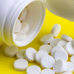 White prescription tablets spilling out of an open pill bottle onto a bright yellow surface, with visible dosage markings.