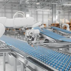 Robotic arm operating over a conveyor belt filled with uniform blue-capped pharmaceutical vials in an advanced automated manufacturing facility.