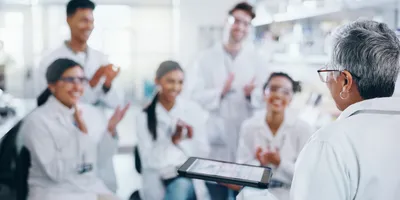Senior scientist presenting data to a group of motivated lab staff applauding in a lab setting.