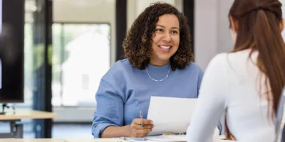 Female lab manager holds onto a resume while speaking with the new hire candidate they are considering.