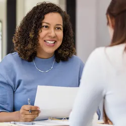 Female lab manager holds onto a resume while speaking with the new hire candidate they are considering.