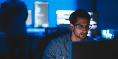 A cybersecurity analyst for a laboratory looks at his computer, with other screens running programs in the background