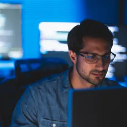A cybersecurity analyst for a laboratory looks at his computer, with other screens running programs in the background