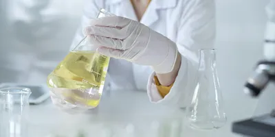 Gloved scientist holding beaker with yellow solvent in teaching lab setting, highlighting safe chemical handling and green chemistry practices for upcoming CHAS Chat event