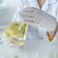 Gloved scientist holding beaker with yellow solvent in teaching lab setting, highlighting safe chemical handling and green chemistry practices for upcoming CHAS Chat event
