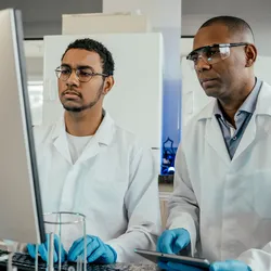 Two lab technicians engaged in on-the-job training at a computer