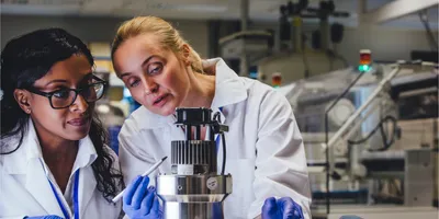Two female scientists in lab coats collaborating over lab equipment, demonstrating teamwork and a quality-first mindset in laboratory operations