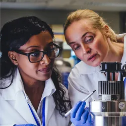 Two female scientists in lab coats collaborating over lab equipment, demonstrating teamwork and a quality-first mindset in laboratory operations