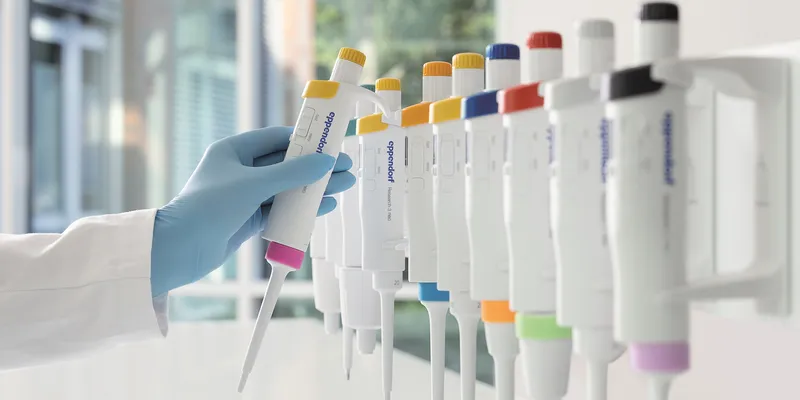 Gloved hand reaching towards a row of colorful pipettes