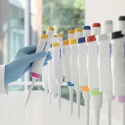 Gloved hand reaching towards a row of colorful pipettes