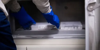 Person wearing protective gloves placing lab freezer boxes into an ultra-low temperature freezer, illustrating cold storage practices. Sustainable cold storage practices are essential to reduce a lab's energy footprint
