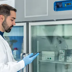 Lab technician checking temperature on medical freezer with tablet
