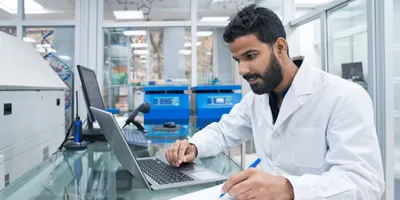 A laboratory scientist works at a computer in a sterile lab environment, representing the implementation of compliant lab software systems.