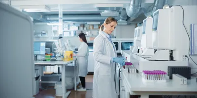 Clinical laboratory scientists in white coats working with automated analyzers and test tubes in a modern medical lab