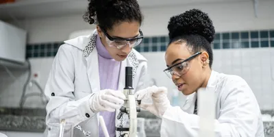 Lab shadowing session between two scientists using a microscope.