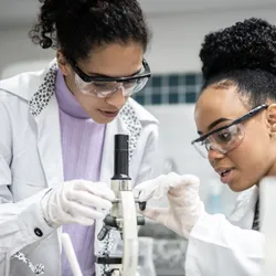 Lab shadowing session between two scientists using a microscope.