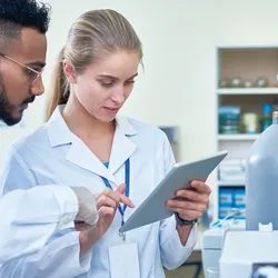 Two lab professionals discussing information on a tablet standing next to lab gas canisters and equipment