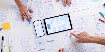 Hands collaborating on mobile and tablet interface wireframes, representing user experience (UX) design principles relevant to LIMS software in laboratory environments.