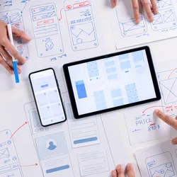 Hands collaborating on mobile and tablet interface wireframes, representing user experience (UX) design principles relevant to LIMS software in laboratory environments.
