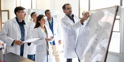 Scientists in lab coats collaborating over a whiteboard in a laboratory setting, highlighting the benefits of generative leadership