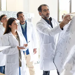 Scientists in lab coats collaborating over a whiteboard in a laboratory setting, highlighting the benefits of generative leadership