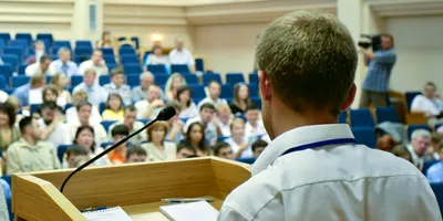 A man is making a speech in front of a big audience at a conference hall.