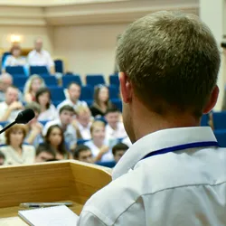A man is making a speech in front of a big audience at a conference hall.