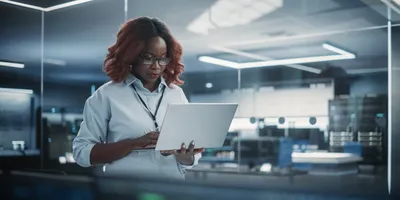 Female lab manager holding laptop and walking around lab while doing cost analysis for the lab