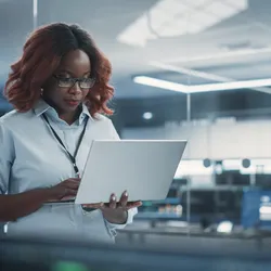 Female lab manager holding laptop and walking around lab while doing cost analysis for the lab