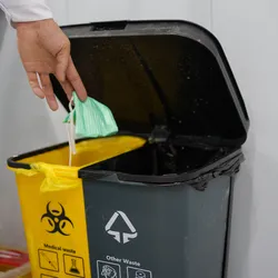 Hand of scientist shown throwing away mask in medical waste container