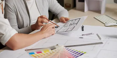 Two people studying a room layout, surrounded by drafting supplies and paint samples