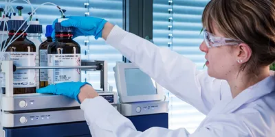 Image of young female scientist in the lab examining solvent bottles for liquid chromatography above an instrument