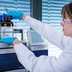 Image of young female scientist in the lab examining solvent bottles for liquid chromatography above an instrument