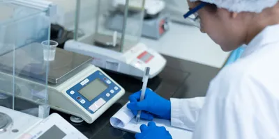 Lab technician weighing liquid for World Quality Week 2025 preparation.