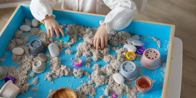 Child playing with colored play sand in a sensory bin