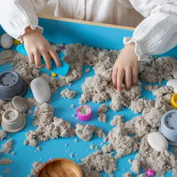 Child playing with colored play sand in a sensory bin