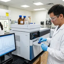 Agricultural laboratory scientist loads samples into LC-MS instrument for pesticide residue analysis with colleague in fume hood.