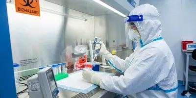 Scientist in PPE handling a biohazard sample inside a biosafety cabinet in a BSL-3 laboratory.