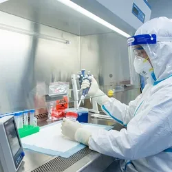 Scientist in PPE handling a biohazard sample inside a biosafety cabinet in a BSL-3 laboratory.