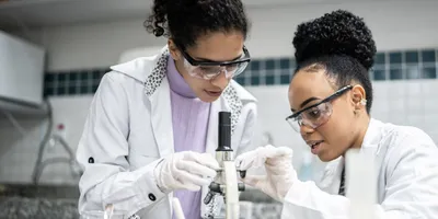 Two women examining a microscope in a lab setting, demonstrating STEM education funding.