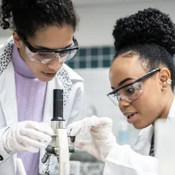 Two women examining a microscope in a lab setting, demonstrating STEM education funding.