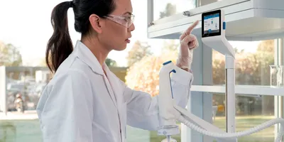 Woman in lab coat and safety glasses using a touch screen